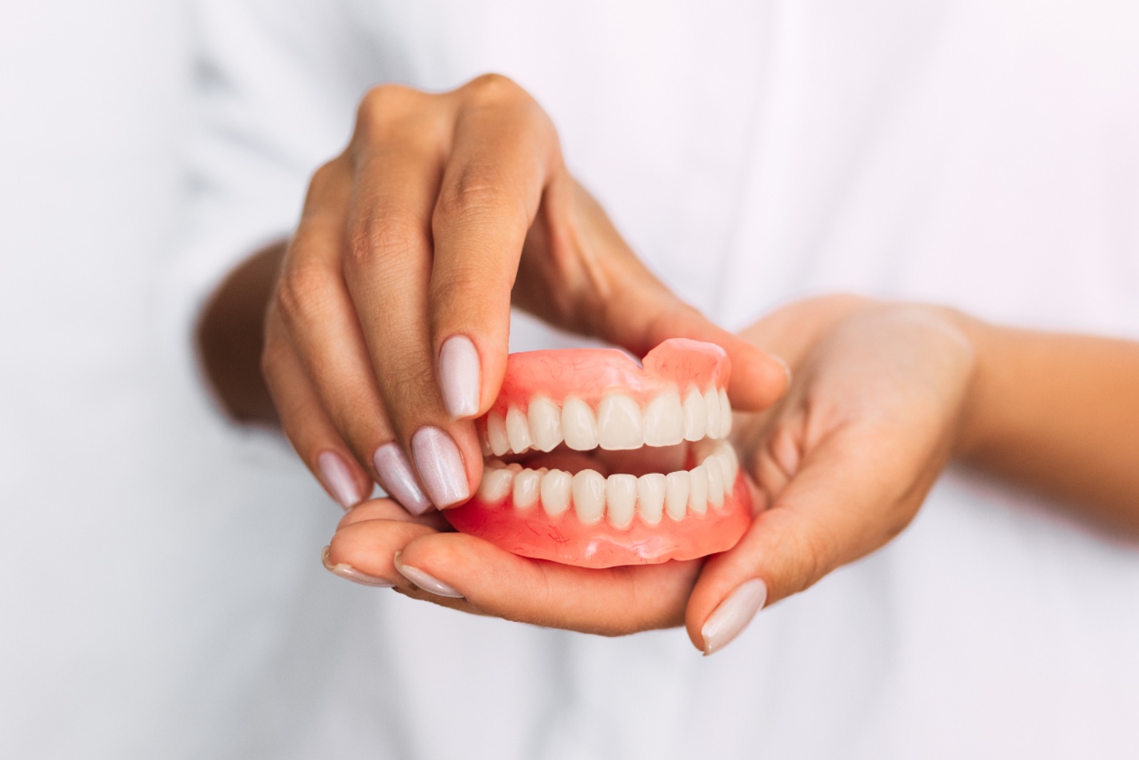 The dentist is holding dentures in his hands. Dental prosthesis in the hands of the doctor close-up. Front view of complete denture. Dentistry conceptual photo. Prosthetic dentistry. False teeth